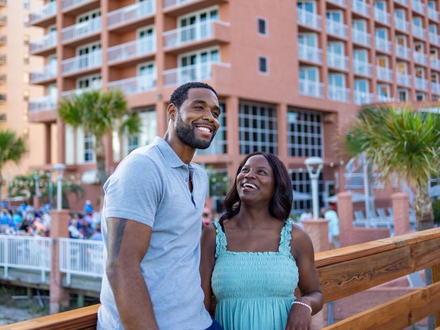 Couple smiling on a boardwalk in front of Perdido Beach Resort in Orange Beach
