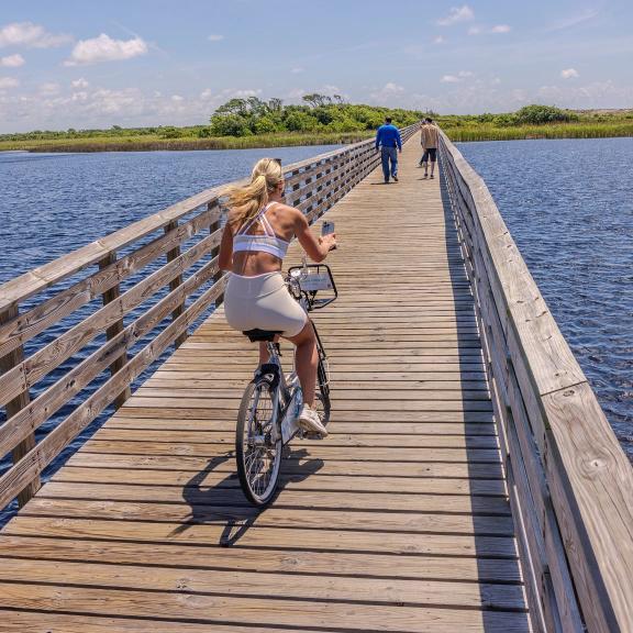 Woman biking on a boardwalk over Lake Shelby in Gulf State Park